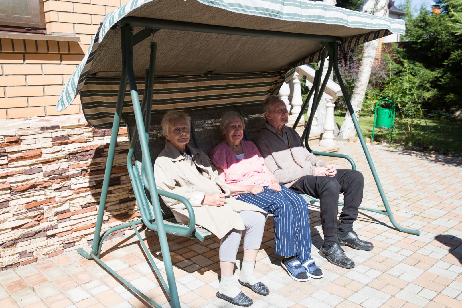 Три пенсионера сидят на садовых качелях